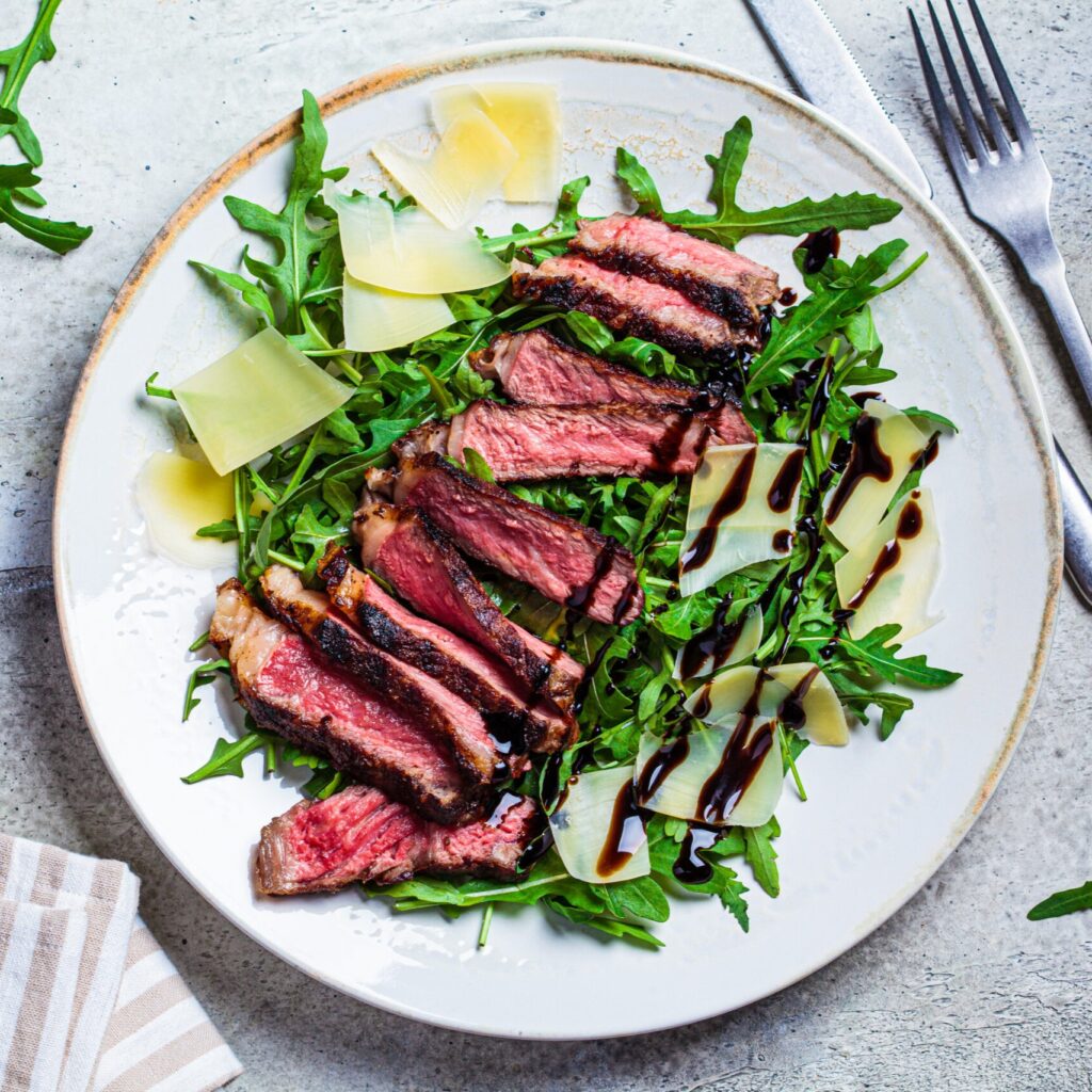 Beef steak tagliata with arugula and parmesan on gray plate, gray background, top view. Italian cuisine concept.